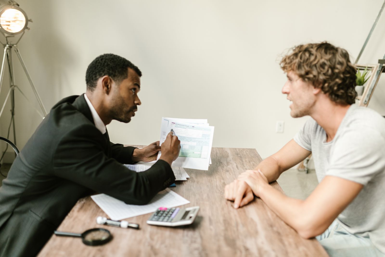 A financial adviser explains tax documents to a client across a wooden desk.